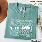 May include: A light green t-shirt with the word "ULTRASOUND" repeated five times in a retro font. The shirt is made of a soft, comfortable material and has a relaxed fit.