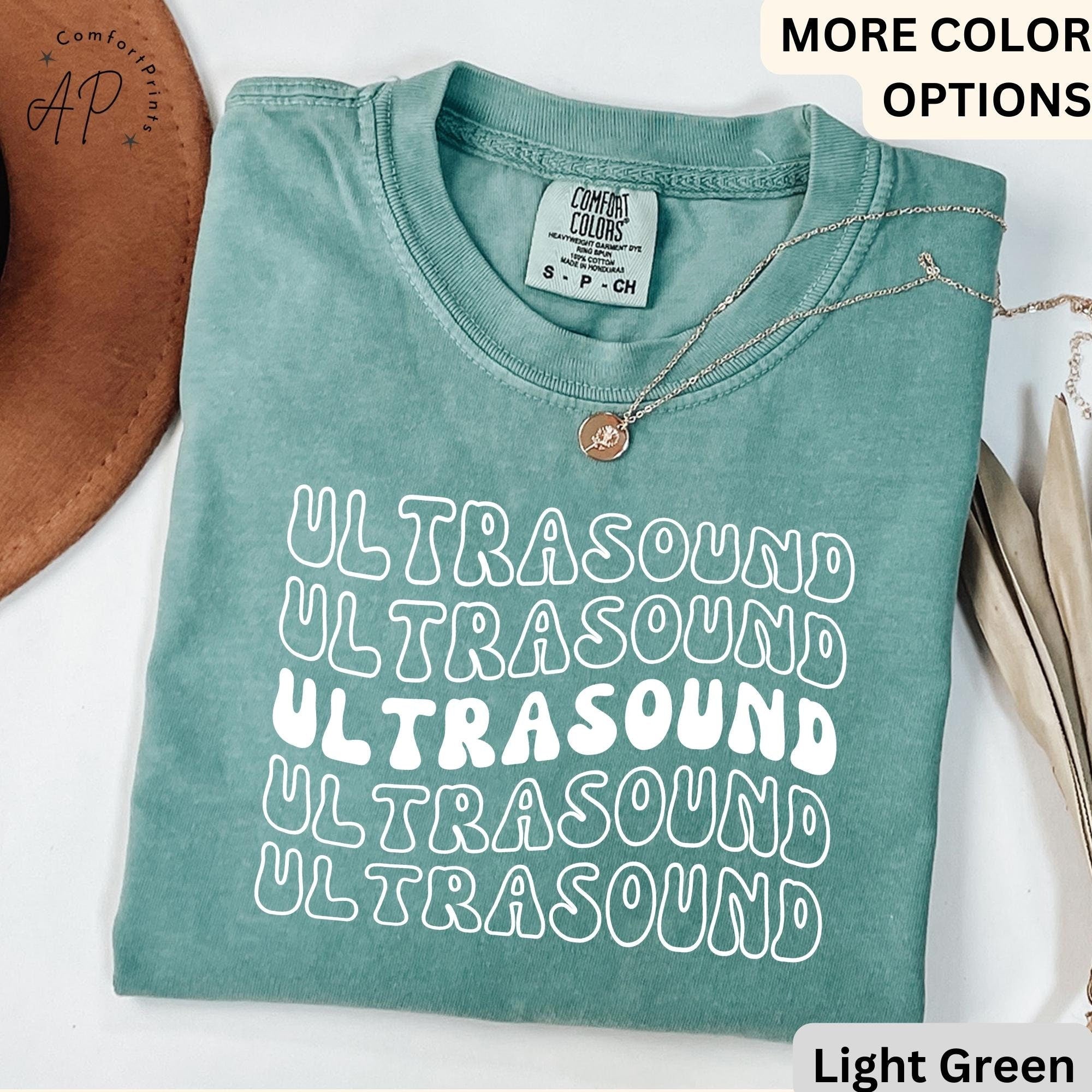 May include: A light green t-shirt with the word "ULTRASOUND" repeated five times in a retro font. The shirt is made of a soft, comfortable material and has a relaxed fit.