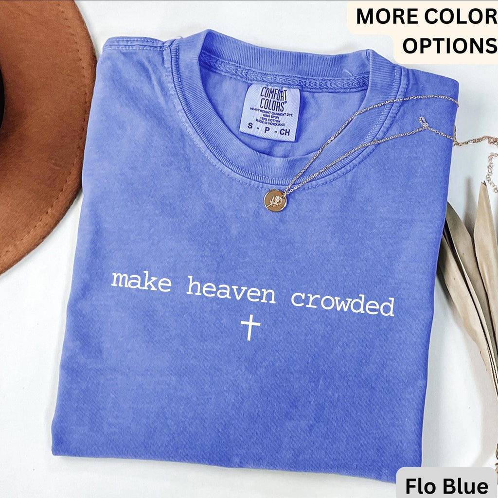 May include: A blue Comfort Colors t-shirt with the phrase "make heaven crowded" and a cross printed in white. A gold necklace with a pendant is draped across the shirt. The shirt is labeled "Flo Blue".
