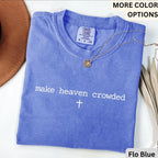 May include: A blue Comfort Colors t-shirt with the phrase "make heaven crowded" and a cross printed in white. A gold necklace with a pendant is draped across the shirt. The shirt is labeled "Flo Blue".