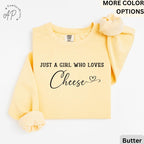 May include: Butter-colored sweatshirt with the text "JUST A GIRL WHO LOVES Cheese" in black script. The sweatshirt has long sleeves and a crew neck. A scrunchie in the same color is on the right sleeve.