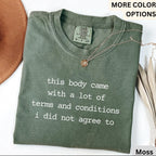 May include: A moss green t-shirt with the text "this body came with a lot of terms and conditions I did not agree to" in white. The shirt has a Comfort Colors tag and is paired with a gold necklace.